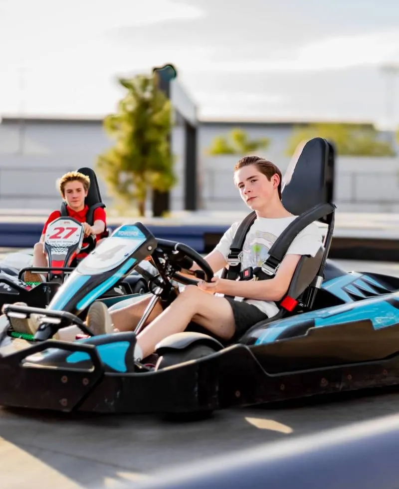 Two people driving black-and-blue go-karts on an outdoor track.