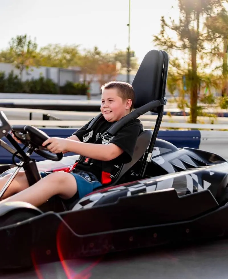 Boy smiling while driving a black go-kart outdoors at sunset