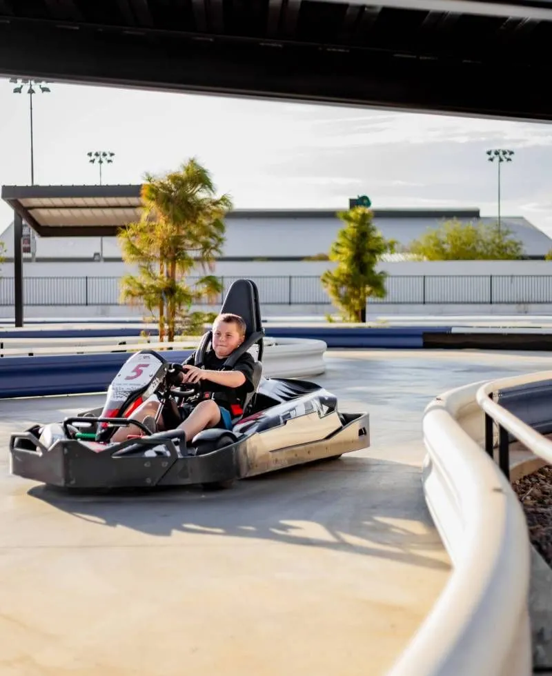 Person driving a go-kart on an outdoor track in bright sunlight