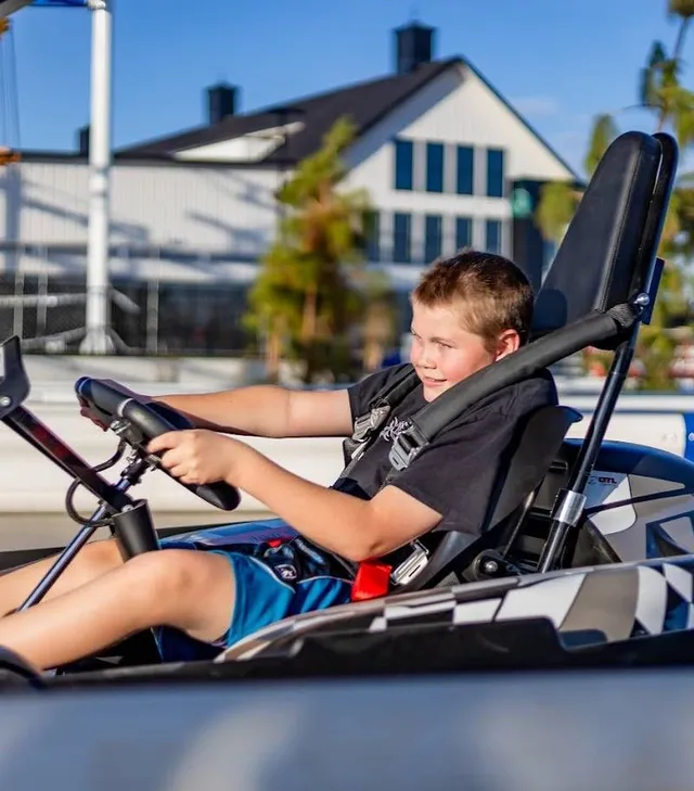 Boy driving a go-kart outdoors on a sunny day, wearing a seat belt and focused on the steering wheel