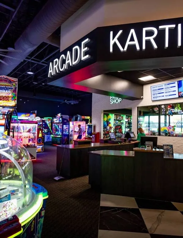 Neon-lit arcade and karting entrance with game machines and counters inside a mall-like venue