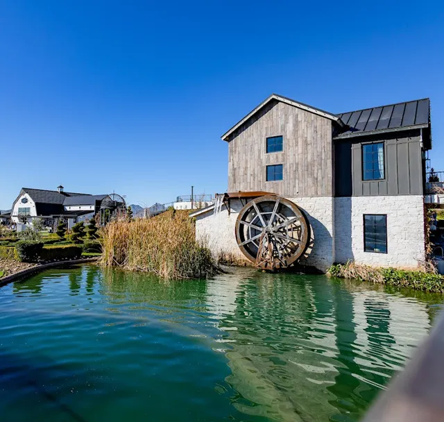 Waterfront mill house with a large wooden water wheel beside a canal under a clear blue sky